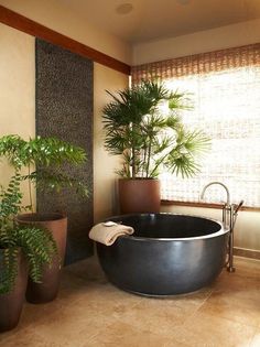 a bath tub sitting in the middle of a bathroom next to two potted plants