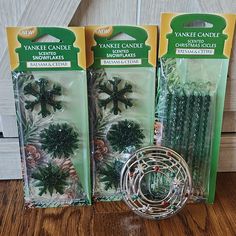 three packaged christmas candles in packaging on a wooden table next to a candle holder and wire