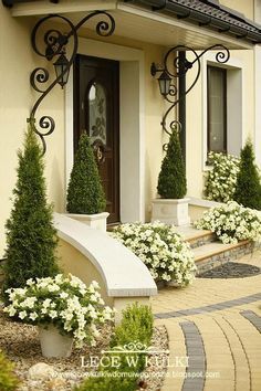 a house with white flowers and bushes in front of the door, on a cobblestone walkway