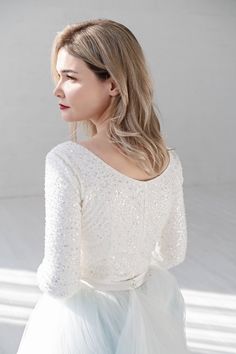 a woman with long hair wearing a white top and tulle skirt, looking off to the side