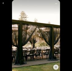 an outdoor dining area with tables and chairs covered in black sheer curtains, surrounded by tall trees