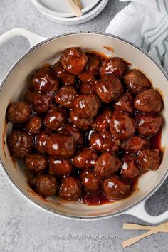 meatballs with sauce in a pan on a table next to chopsticks and bowls