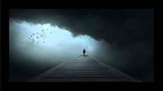 a person standing on top of a wooden pier under a dark sky with birds flying overhead