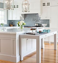 a white kitchen with an island and chandelier hanging from it's ceiling