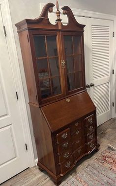 an old wooden china cabinet with glass doors on the top and bottom, sitting in front of a white door