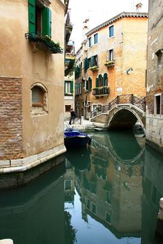 a small boat is floating in the water near buildings and a bridge with green shutters