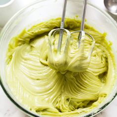 a mixing bowl filled with green cream and two metal whisks in it,