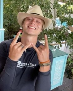 a young man wearing a hat making the peace sign with his fingers while sitting at a table