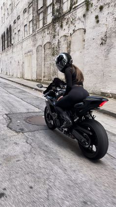 a woman riding on the back of a black motorcycle down a street next to tall buildings