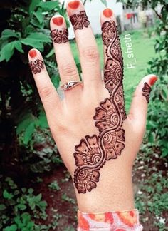 a woman's hand with henna tattoos on her left arm and fingers, in front of some bushes