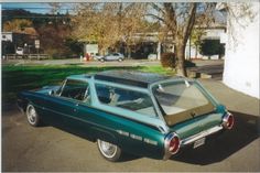 an old green car parked in a parking lot next to a tree with no leaves on it