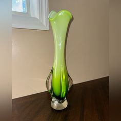 a green vase sitting on top of a wooden table next to a white framed window