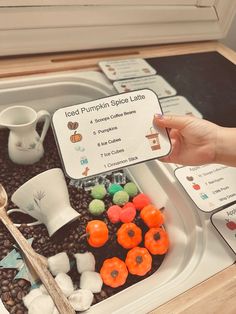 a person is holding a card in front of a tray filled with fake pumpkins and marshmallows