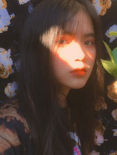 a woman with long black hair standing in front of flowers