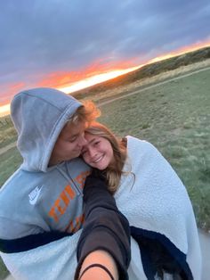 a woman wrapped in a blanket is taking a selfie with her cell phone at sunset