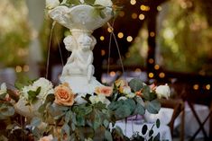 an arrangement of flowers and greenery is displayed in front of a table with lights