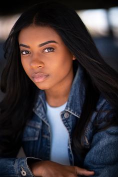 a woman with long black hair wearing a denim jacket and white t - shirt looking at the camera