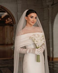 a woman in a white wedding gown holding a bouquet of flowers and wearing a veil