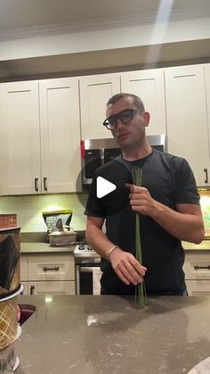 a man standing in front of a kitchen counter holding up some green plants to eat