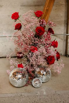 red roses and baby's breath in a silver vase with disco balls on the floor