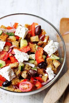 a glass bowl filled with vegetables and croutons on top of a wooden spoon