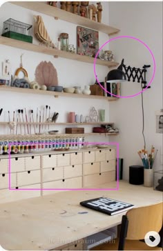 a wooden table topped with lots of crafting supplies next to shelves filled with items