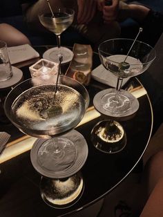 three martini glasses sitting on top of a glass table filled with different types of drinks