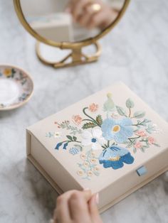 a person holding a box with flowers painted on it and a mirror in the background