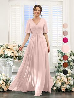 a woman standing in front of flowers wearing a long pink bridesmaid dress with short sleeves