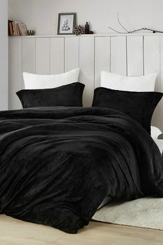 a black comforter set with white pillows on a bed in front of a wooden headboard