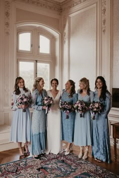 a group of women standing next to each other in front of a window holding bouquets