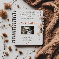 a baby book is laying on top of some dried flowers and blankets, with the title we are adding a new chapter to our love story