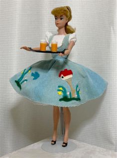 a doll holding a tray with a drink on it's arm and wearing a blue dress