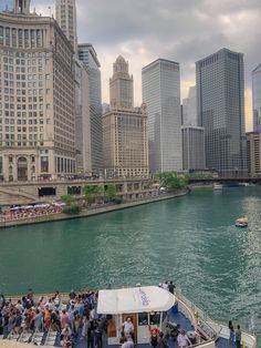 people are standing on the deck of a boat in the water near tall buildings and skyscrapers