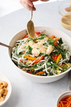 a person holding a spoon over a salad in a bowl with carrots and cashews