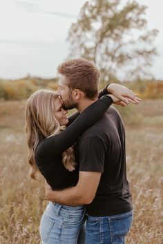 a man and woman embracing each other in the middle of a field with tall grass