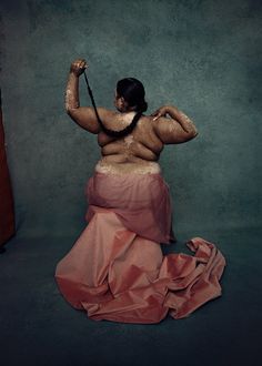 a woman in a pink dress with her back turned to the camera, holding an umbrella