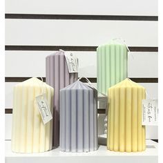 four different colored candles sitting on top of a white shelf with tags attached to them