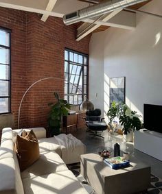 a living room filled with lots of furniture next to large windows on top of a brick wall