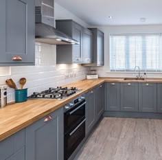 a kitchen with grey cabinets and wooden counter tops, along with a stove top oven