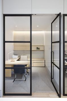 an office with glass walls and desks in the center, looking out to another room