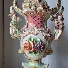 an ornate vase with figurines and flowers on the bottom is shown in front of a white wall