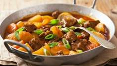 a pot filled with meat and vegetables on top of a wooden table next to a spoon