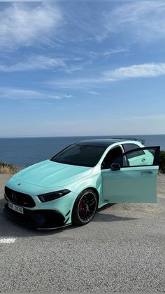 a blue car parked on the side of a road next to the ocean