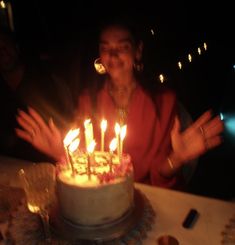 a woman sitting in front of a cake with lit candles