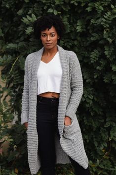 a woman standing in front of a bush wearing a white top and grey cardigan