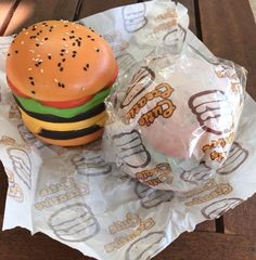 a hamburger and a burger wrapped in plastic wrapper sitting on top of a wooden table