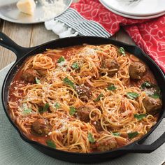 a skillet filled with spaghetti and meatballs on top of a wooden table next to silverware