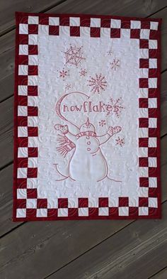 a red and white quilted wall hanging on the side of a wooden floor with snowflakes