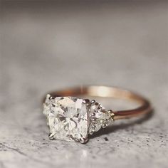 an engagement ring with three stones on it sitting on a stone surface in front of the camera